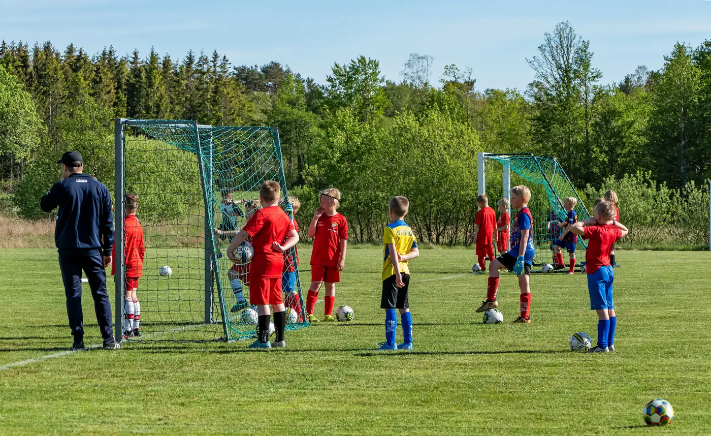 Children at a summer sports camp playing football on a sunny pitch
